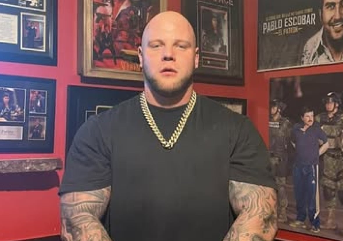 A bald man in a black t-shirt wearing a gold chain.