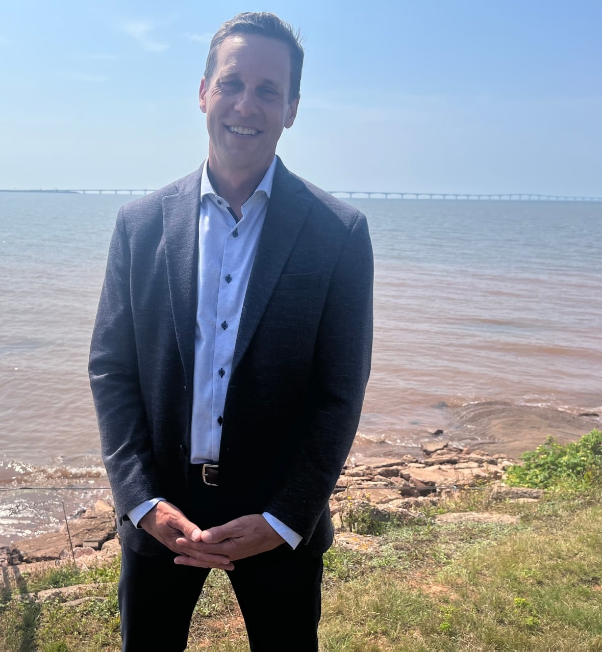A man standing on a shoreline with a large bridge in the distant background.