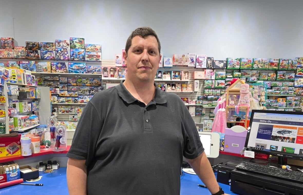 Person standing at checkout, looking at the camera, there are shelves of toys in the background.