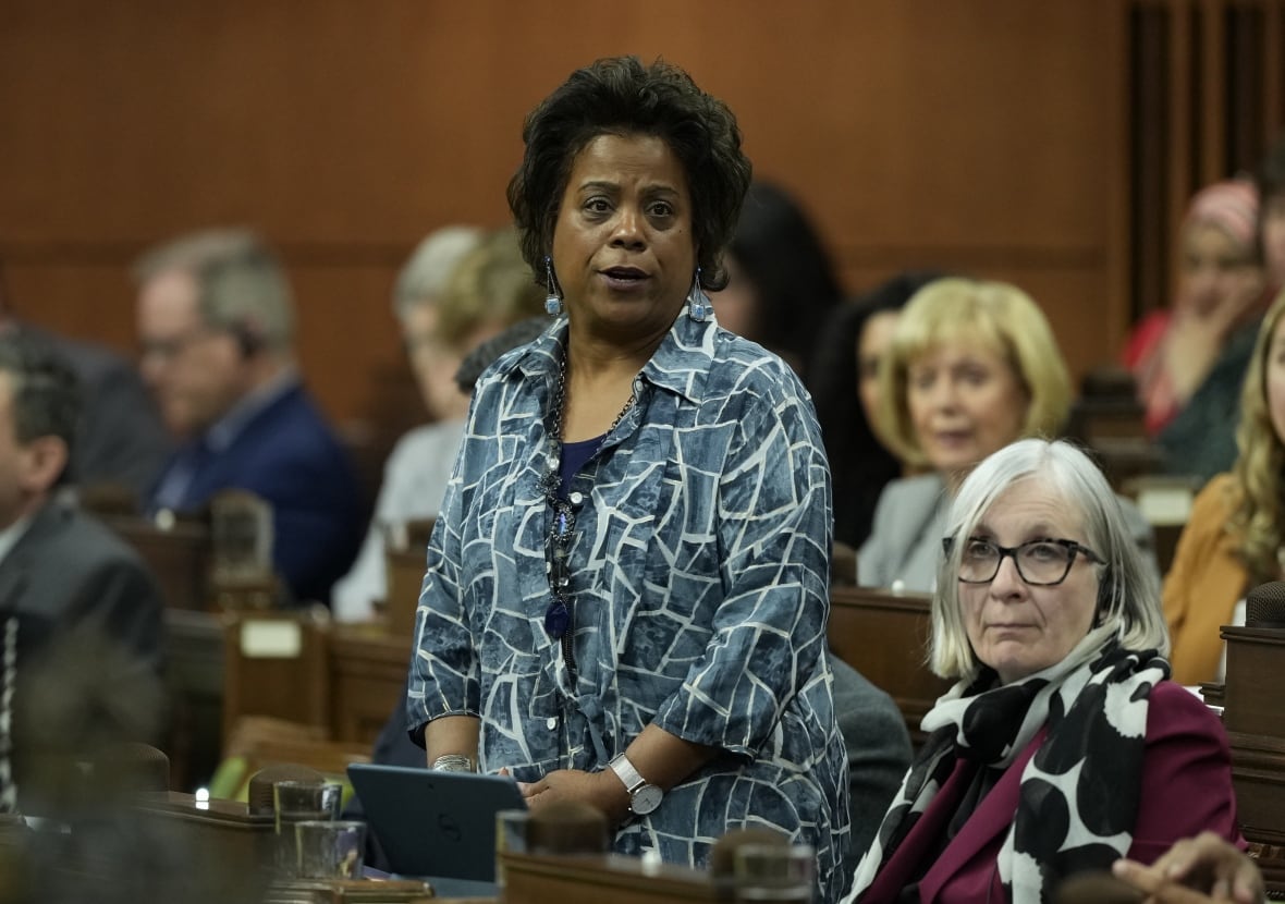 A woman in a patterned blazer stands and speaks in the House of Commons.