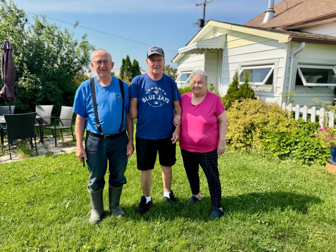 Two men and a women stand in front of a house smiling.