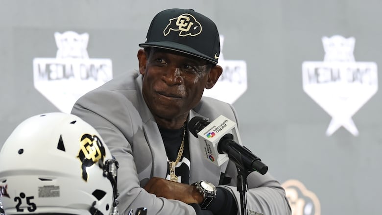 A man sits, speaking to the media.