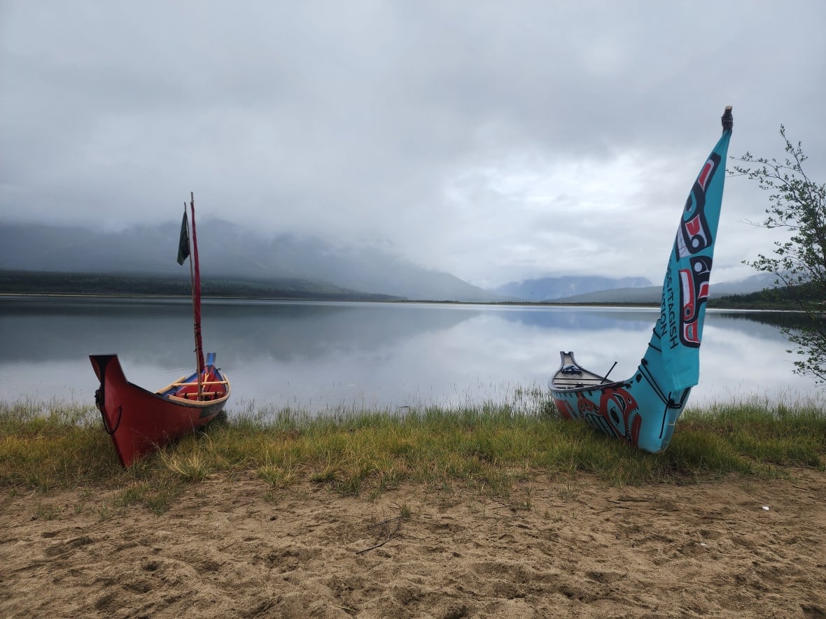 Two canoes, one blue and one red, sits on the shore.