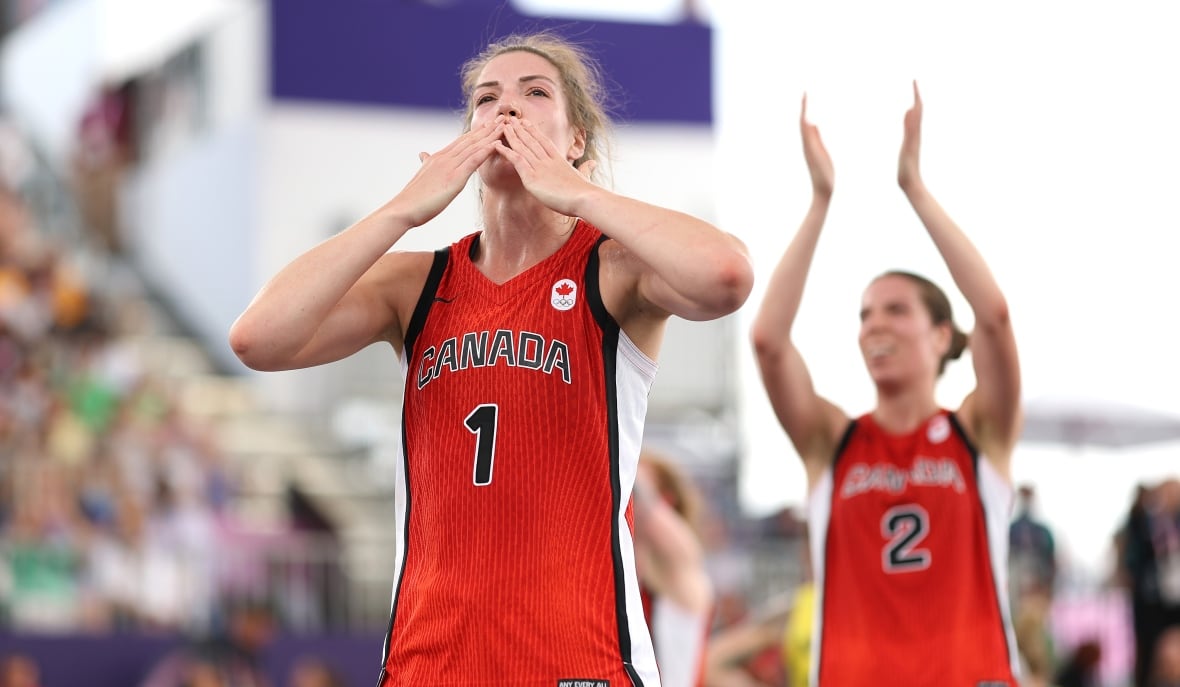 Eine Basketballspielerin mit der Nummer eins wirft bei einem Spiel der Menge einen Kuss zu, während Teamkollegen hinter ihr klatschen.