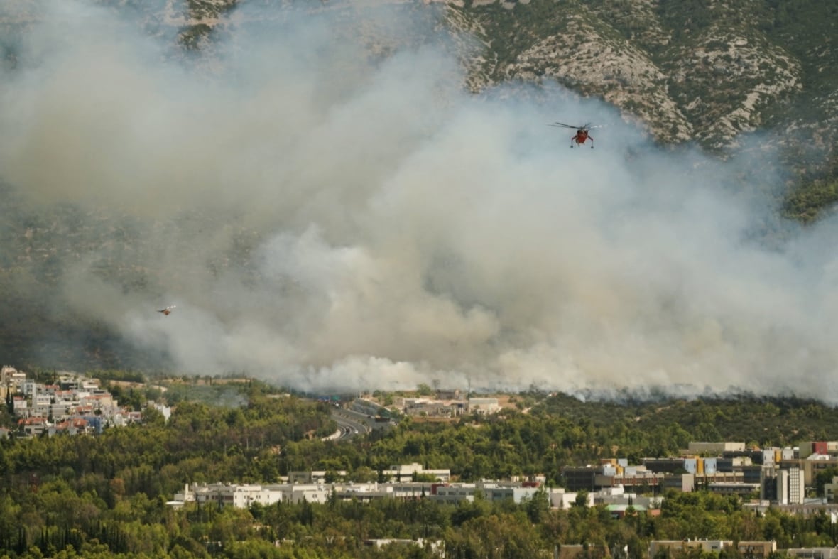 A firefighting helicopter is seen amidst grey smoke above a forested area