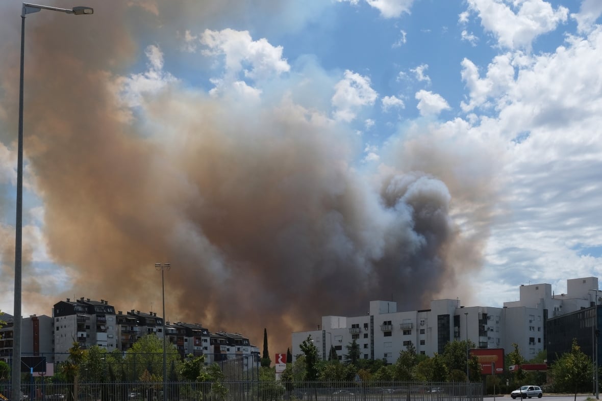 A huge cloud of smoke coming up from a city block of apartment buildings against a blue sky