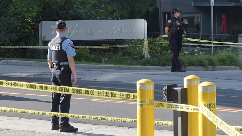 two police stand on road with caution tape