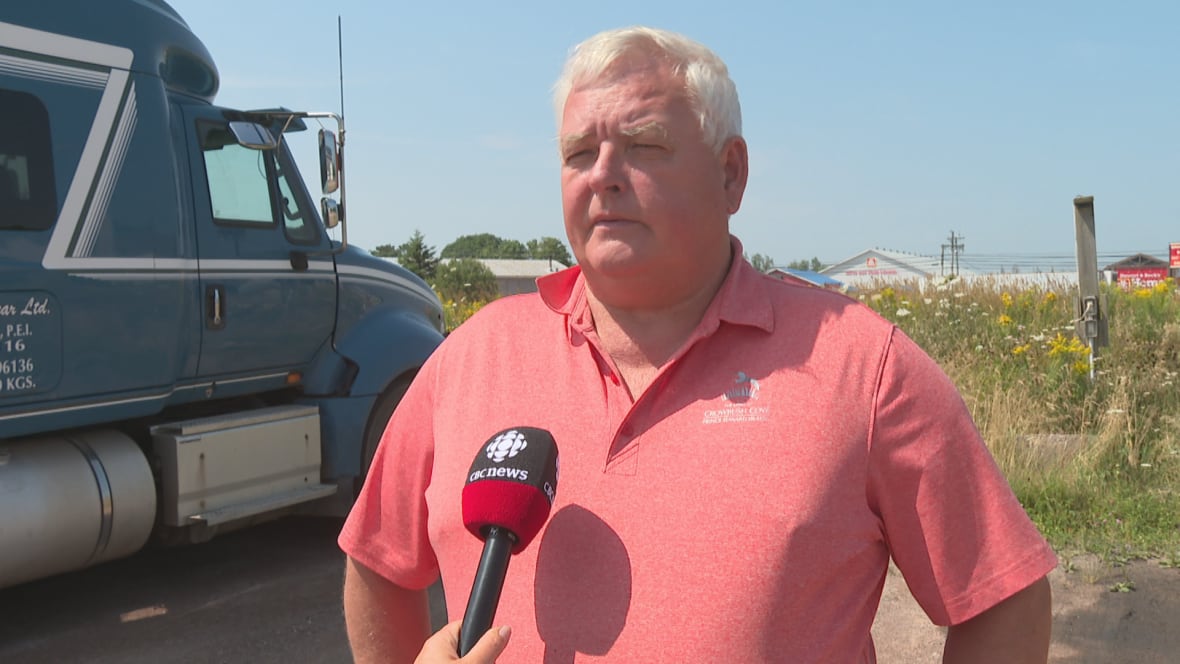 A man in a pink shirt stands next to a large truck.