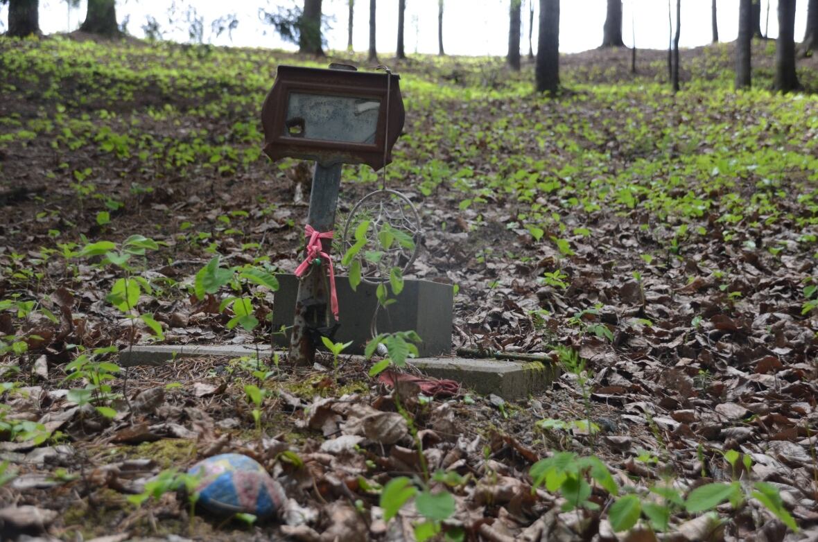 A grave marker in a forested area with a painted rock and a dream catcher 