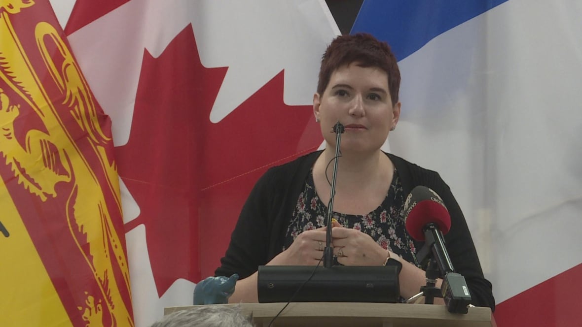 A woman with short hair speaks at a podium.