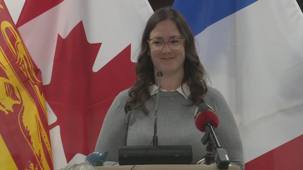 A woman with long brown hair speaks at a podium.