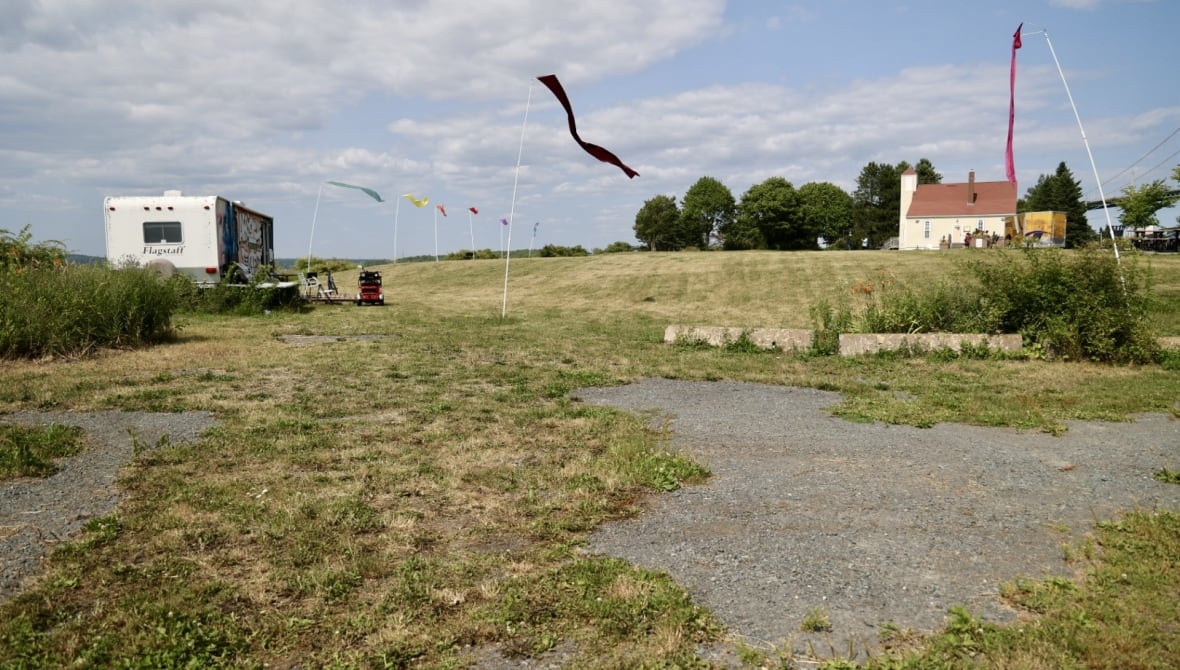 A trailer is seen on the left sitting on a grassy field, with a replica church near by