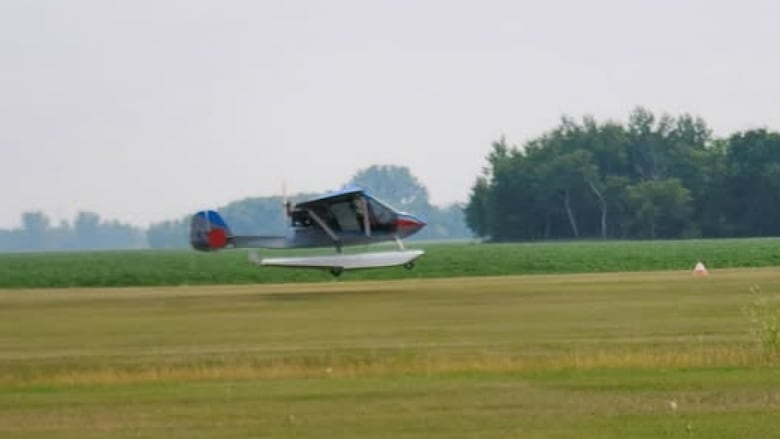 Small blue, red and white airplane viewed from across a green field.