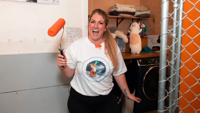 A woman stands holding a paint roller.