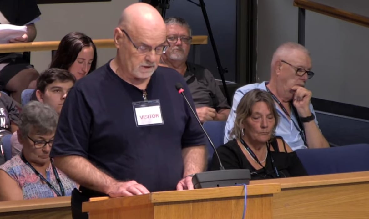 Bolohan speaking at the podium with spectators seated behind him.