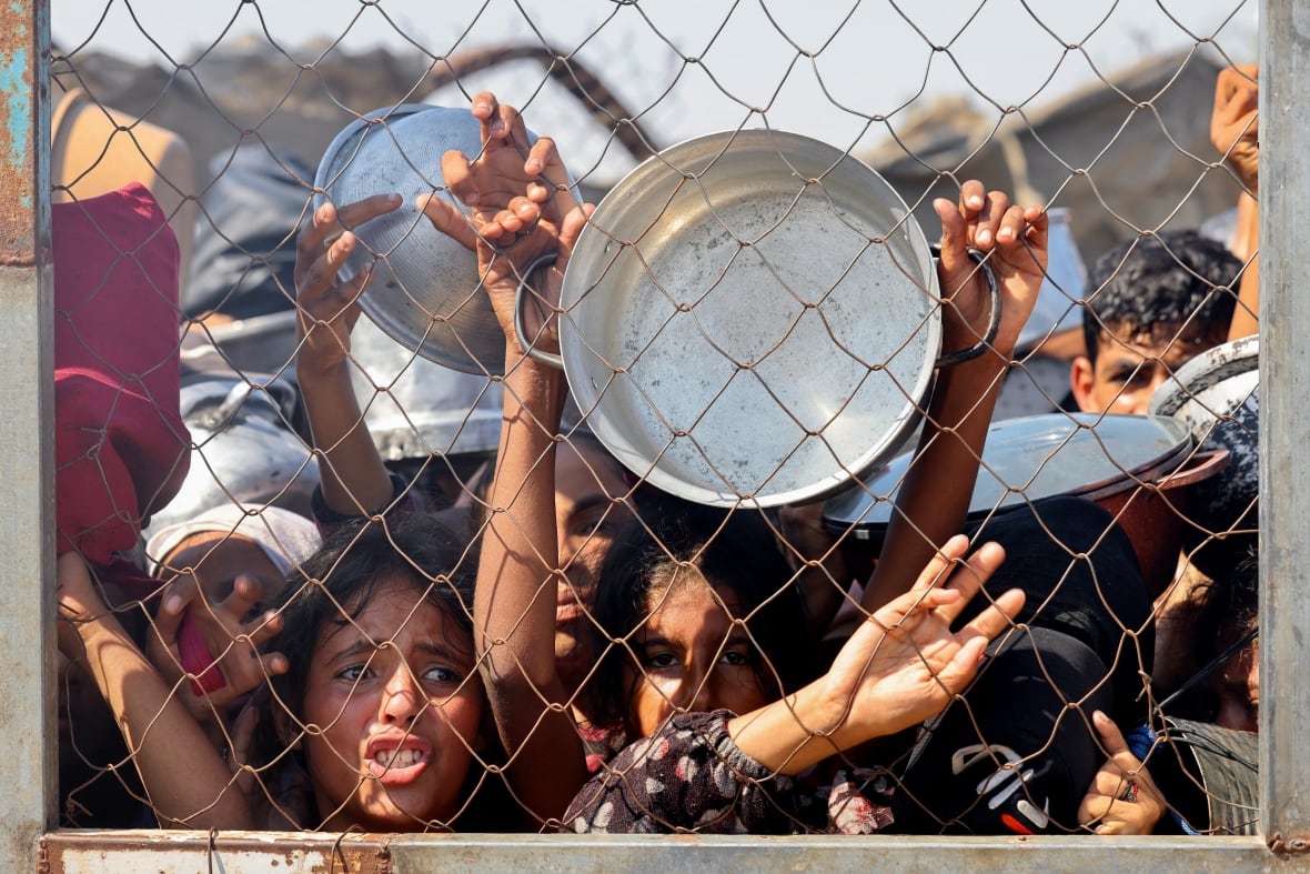 A group of mainly children push against a chain-link fence.