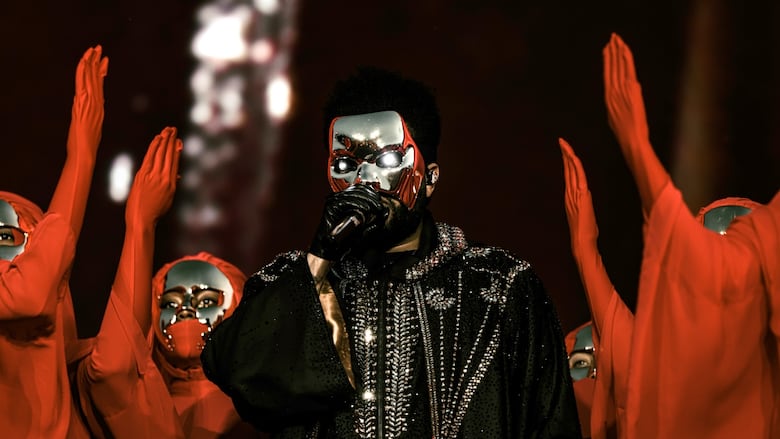 The Weeknd performs flanked by dancers dressed in red veils and gold masks.