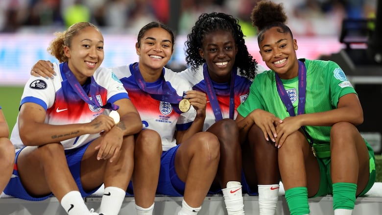 Four soccer players sit and show off medals.