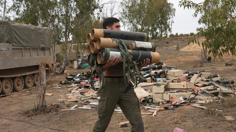 A soldier carries a half-dozen mortar shells.
