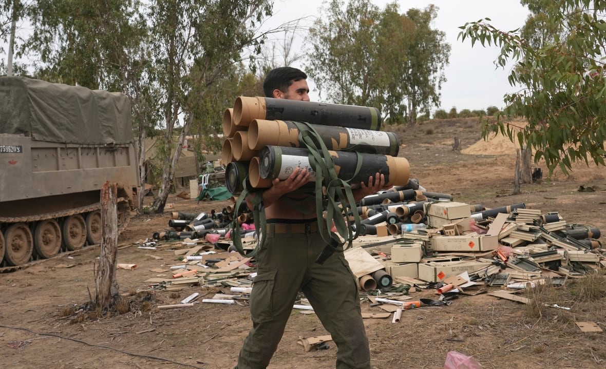 A soldier carries a half-dozen mortar shells.