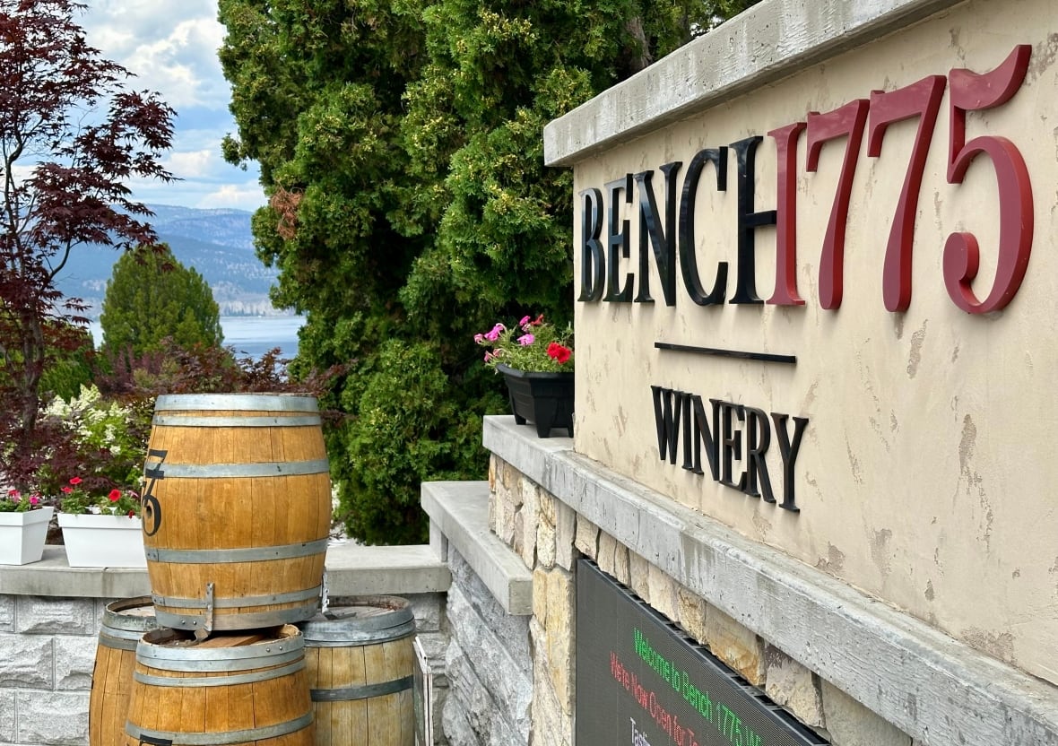 A stone and brick sign is shown outside of a winery with decorate wood barrels nearby.