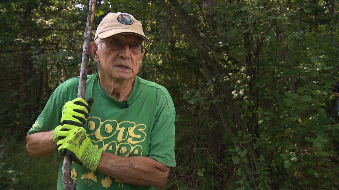 A man with a had stands while holding a long stick.