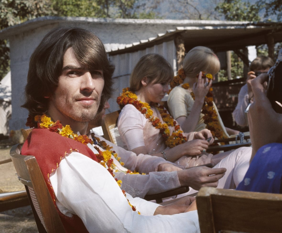 A man in a flower garland looks into the camera with other people in flower garlands in the background.