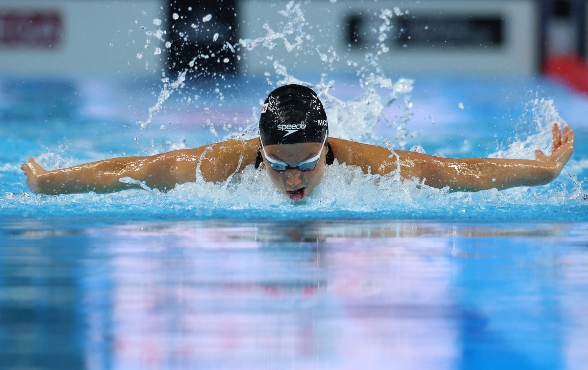 A woman in swim cap and goggles, in a pool, doing a butterfly stroke.