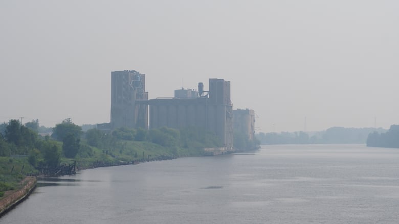 Smoky brick buildings are seen in the distance, with water in the foreground.
