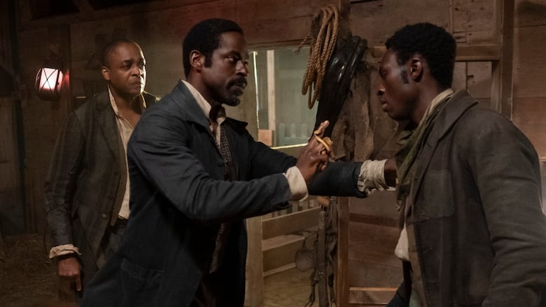 Three well dressed men stand inside a stable, standing as if they are trying to avoid a conflict.