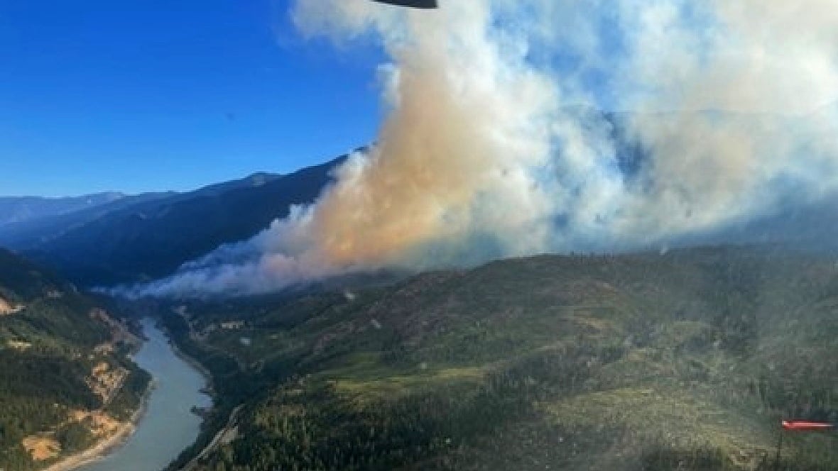 A plume of smoke is seen from the air over a green valley with a river running through it.
