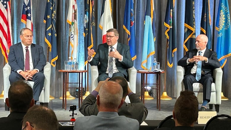 Three people sit in chairs on a stage during a panel discussion in an auditorium.