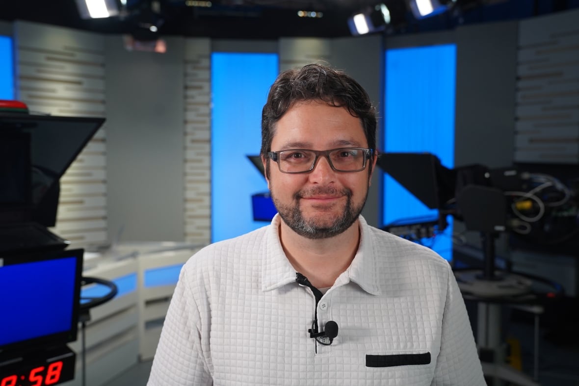 Christopher Gareau, wearing a white shirt, in a tv studio smiling to camera