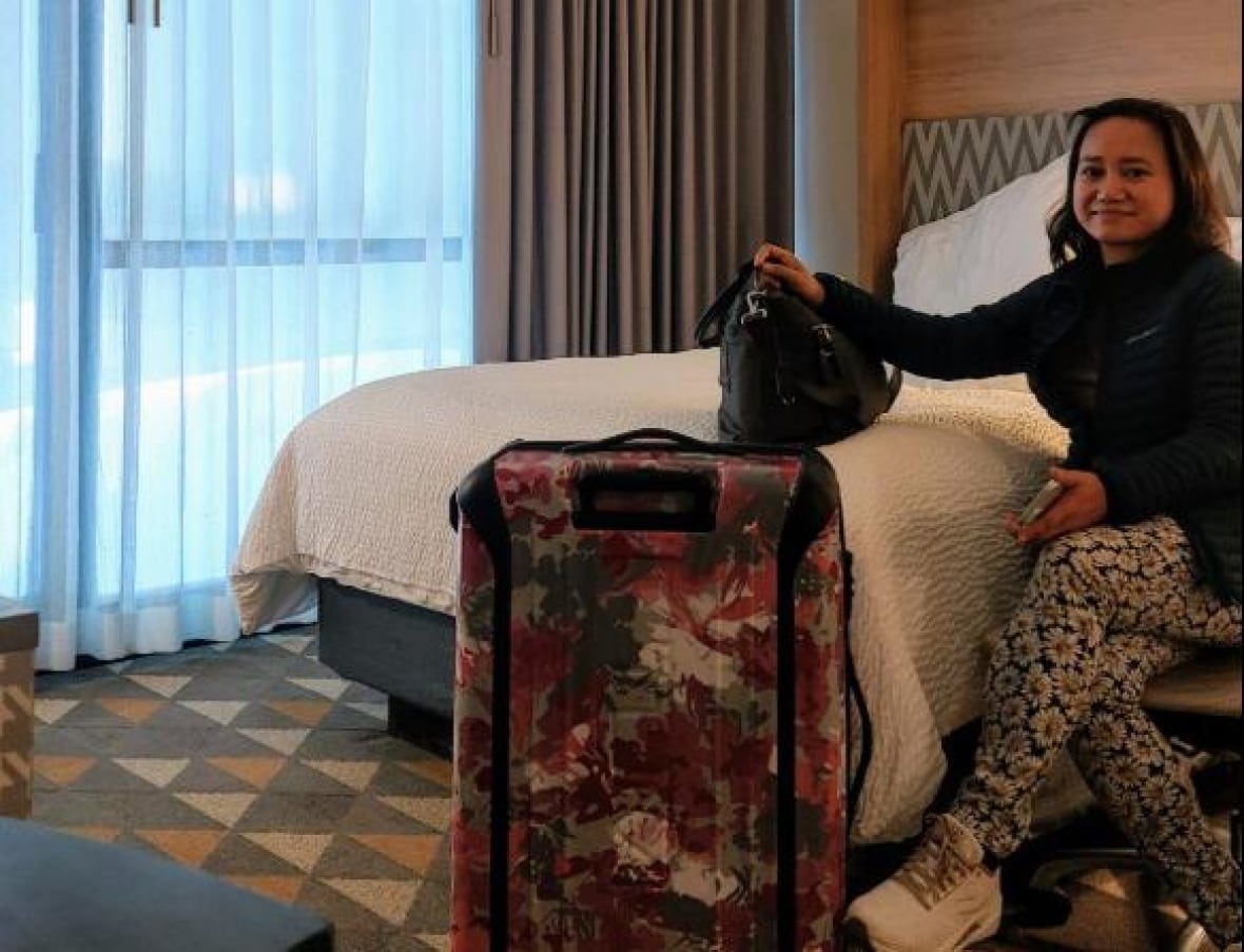 A woman sits on a hotel bed with her luggage next to her. 