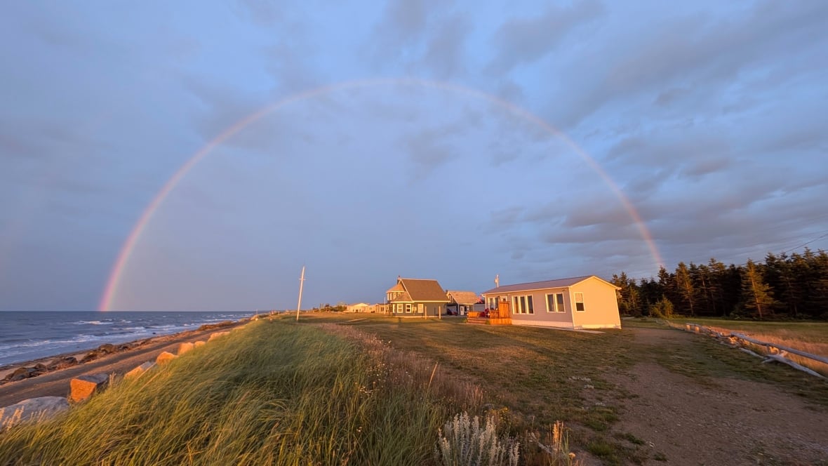 A house on a shoreline with a rainbow in the sky above