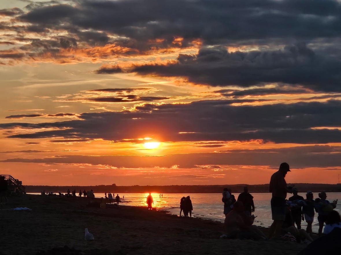 A beach filled with silhouettes of people watching an orange sunset