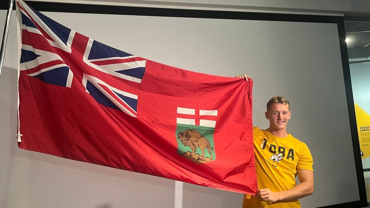 A man poses with the flag of Manitoba. 