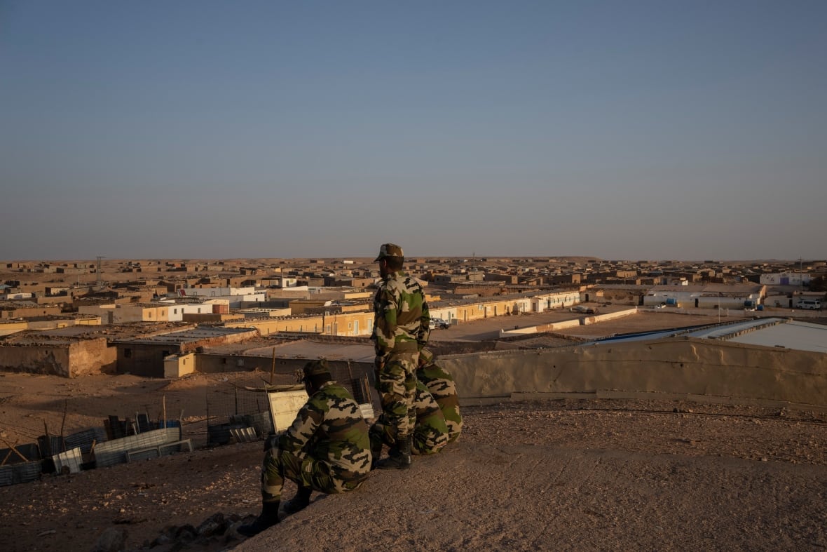 Un soldado en un camuflaje verde se volvió detrás de él, junto a los dos soldados sentados en los soldados cansados, en la colina arenosa frente al refugio en el campo de refugiados.