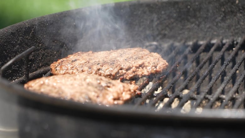 Two beef patties sizzle on an outdoor charcoal grill in the summer