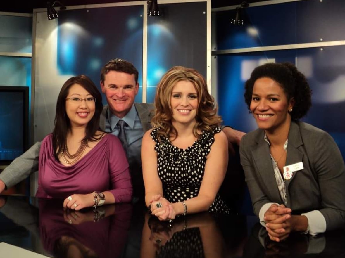 One man and three women pose for a photo together in a news studio.