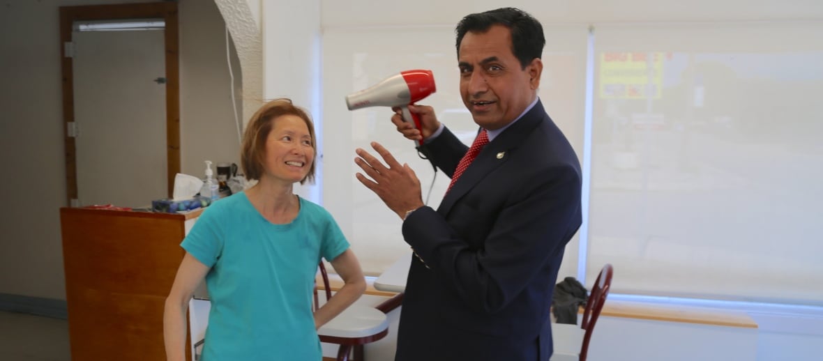 Two people standing up in a hair salon while one blow dries the other's hair