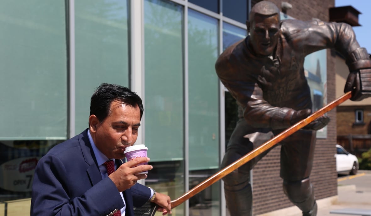 A person sips a coffee in front of a statue of a hockey player