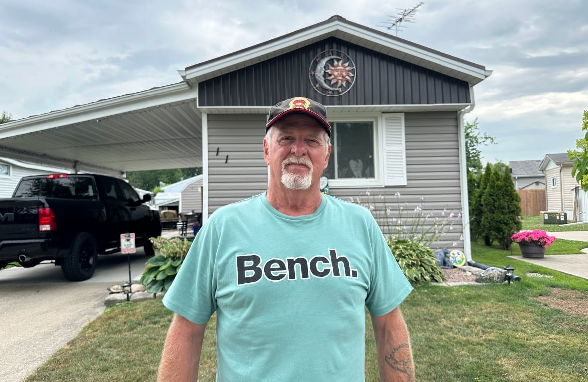 A man in a teal bench shirt standing in front of his house.