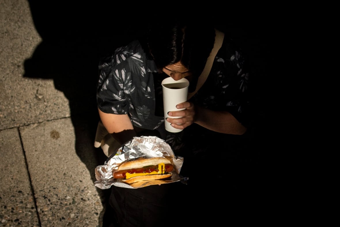 A person holds a hot dog and sips adrink