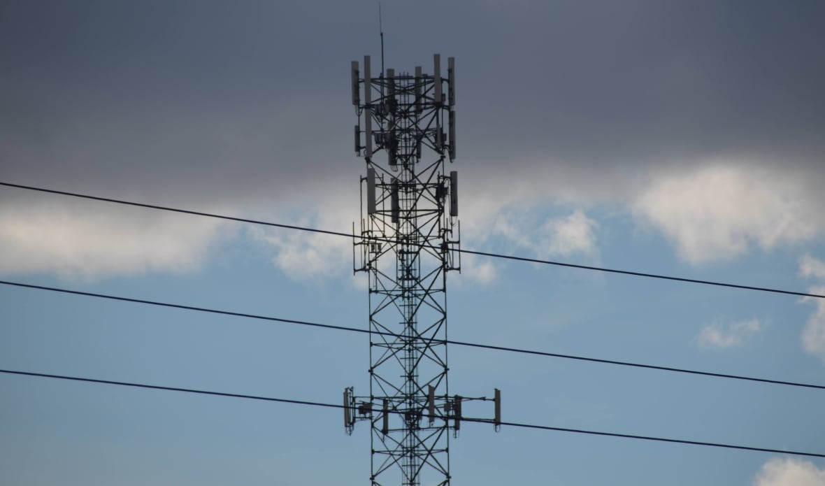 A cellular tower with telephone wires and clouds 