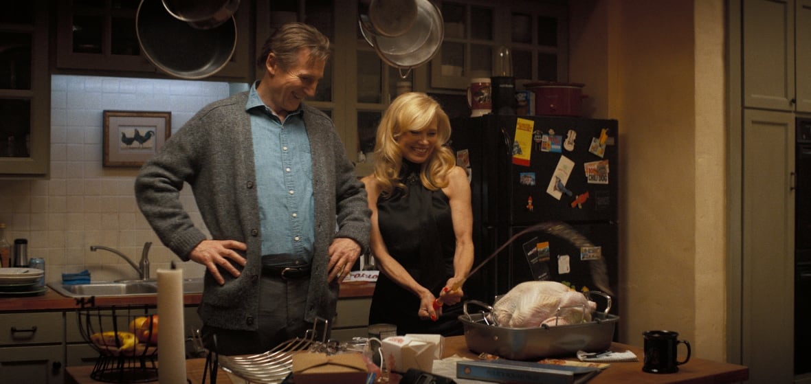A man and woman laugh while basting a turkey. 
