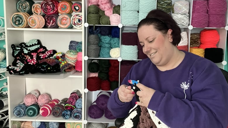 A woman crochets with a wall of yarn behind her