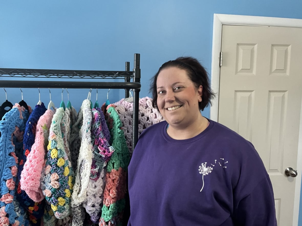 A woman stands next to handmade cardigans