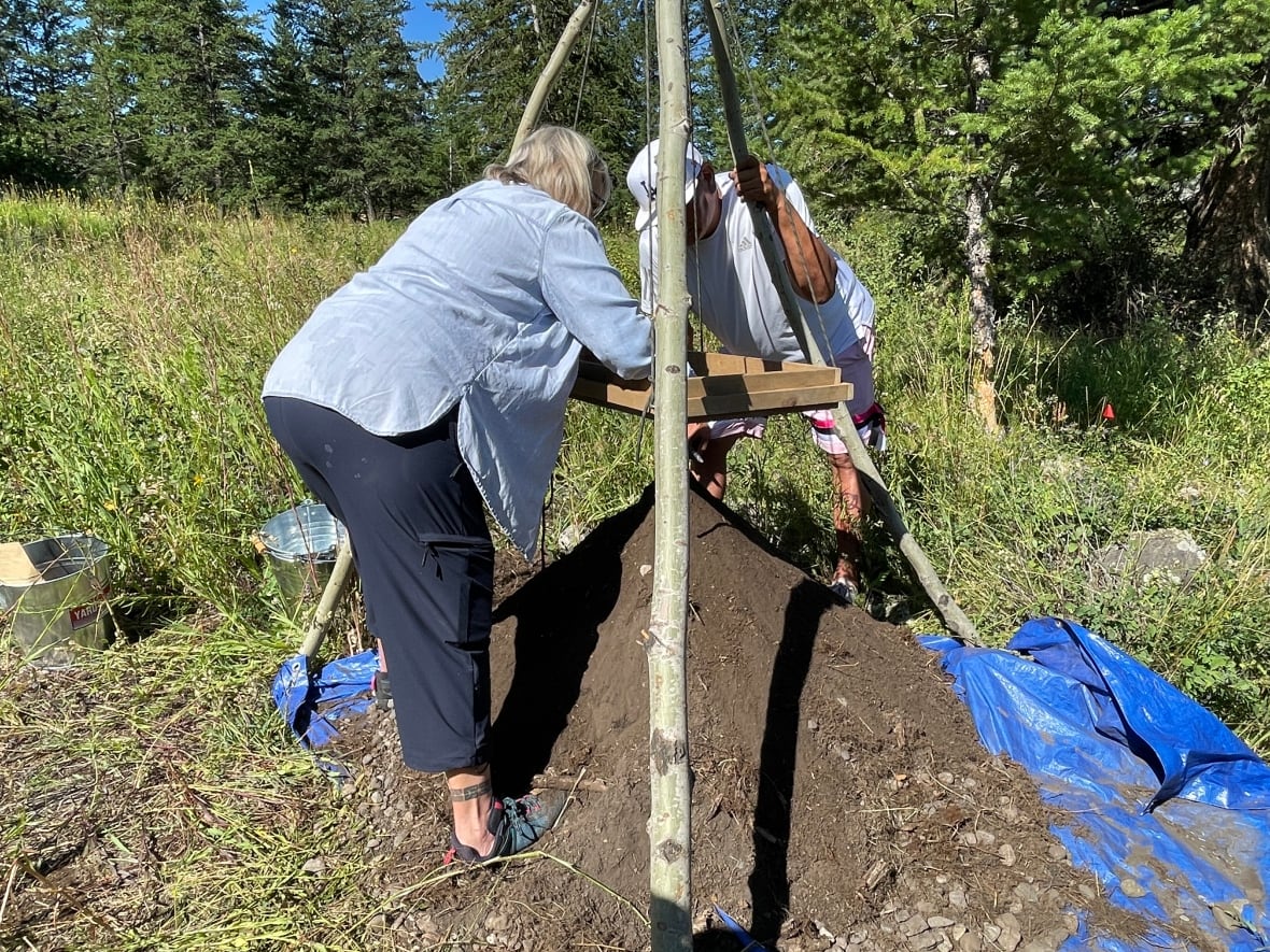 A man and a woman use a sifting apparatus to look through dirt.