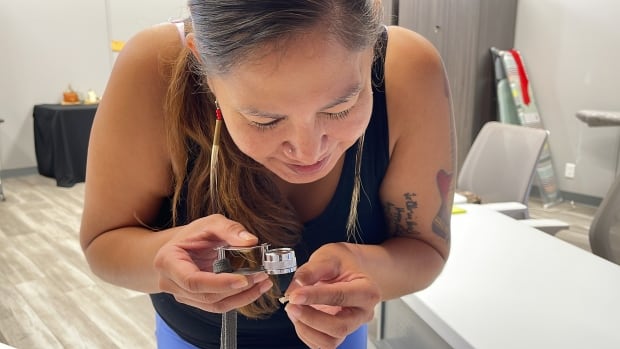 A woman holds a small artifact under a magnifying glass.